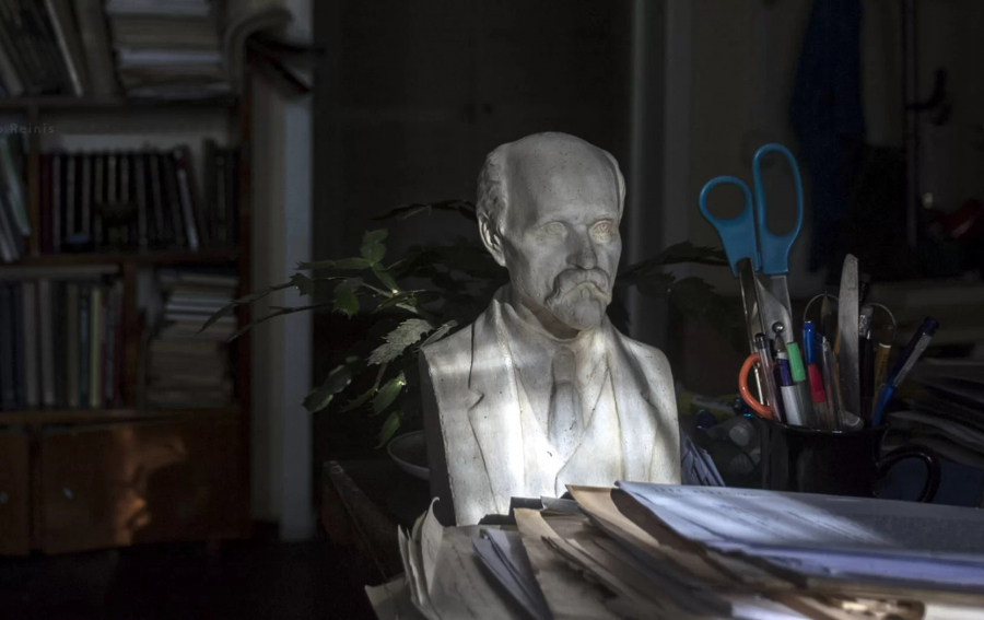 A portrait sculpture that sits on a desk among papers, stationery and books