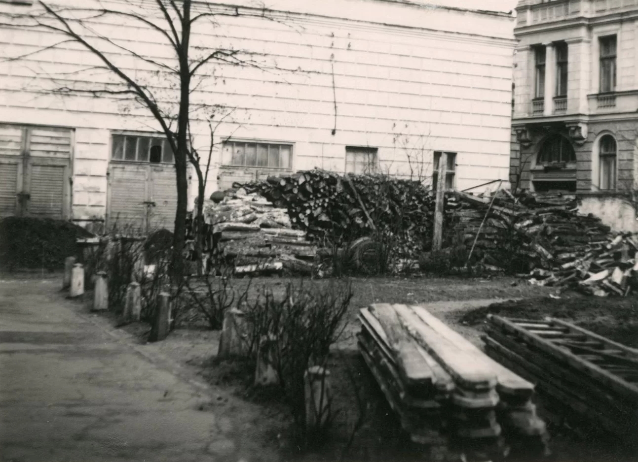 Fotogrāfija no ēkas celšanas procesa. Tajā redzama šķietami malka, kāpnes un garākas pagales uz zemes.