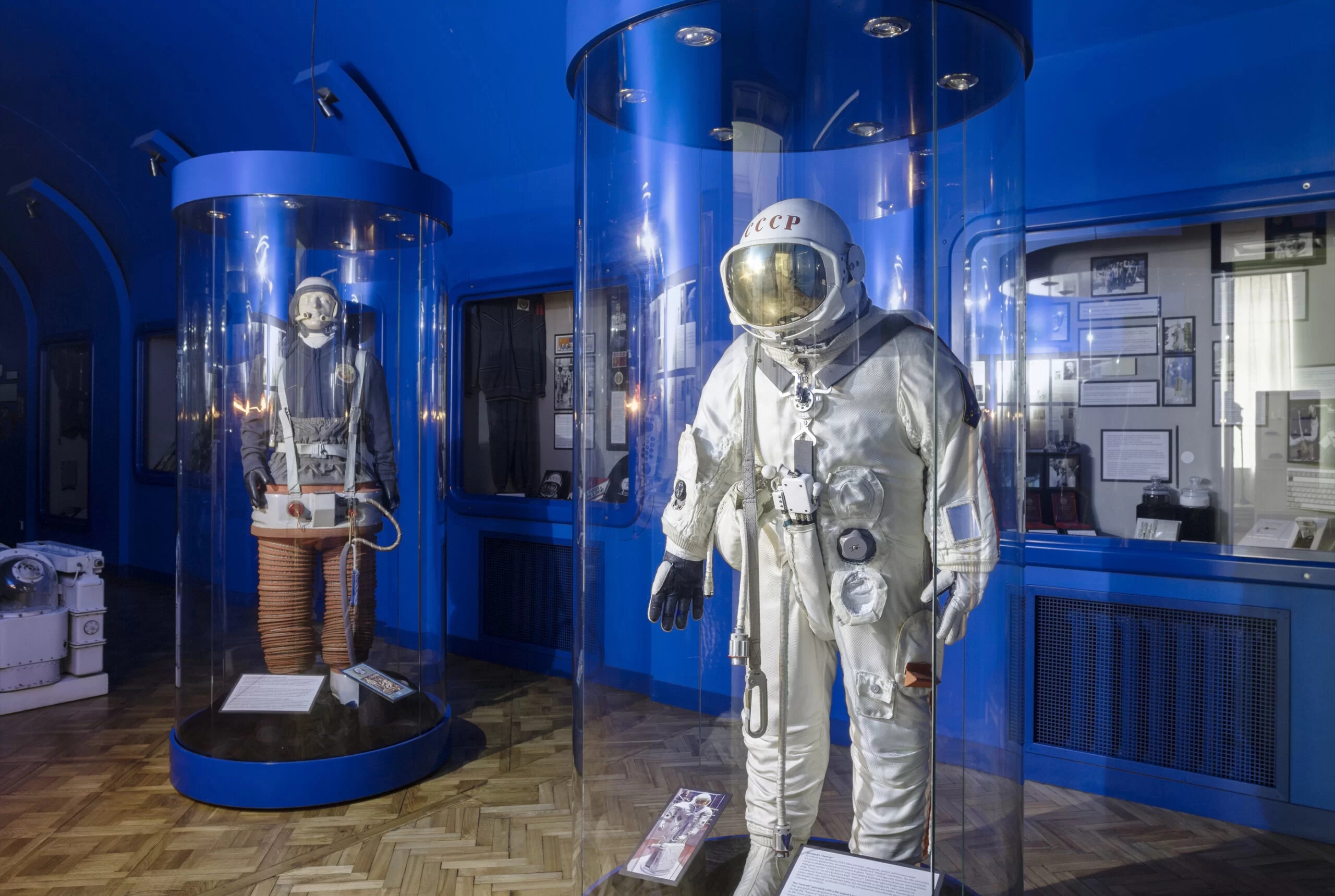 Fotogrāfija no muzeja kosmosa ekspozīcijas, kurā redzami divi astronauta tērpā ģērbti manekeni. Fonā zilas sienas uz kurām atrodas dažādas informatīvas planšetes un ekspozīcijas vitrāžas ar eksponātiem.